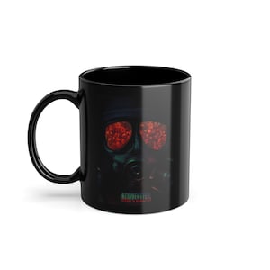 May include: Black ceramic mug with a gas mask design, red lenses, and a green filter. The mug has the text "RESIDENT EVIL" and "WELCOME TO RACCOON CITY". The mug has a curved handle. The mug is suitable for hot beverages.