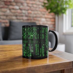 Könnte beinhalten: Schwarze Keramik-Kaffeetasse mit grünem Matrix-Code-Design und dem Text "name here." auf der Vorderseite.