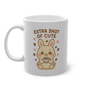 May include: White ceramic coffee mug with the text "EXTRA SHOT OF CUTE" and a cartoon bunny holding a cup of coffee. The design includes coffee beans and hearts in shades of brown and pink.