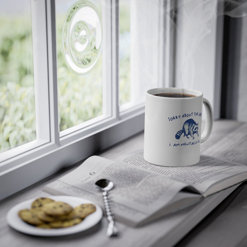 White ceramic mug with funny raccoon meme and caption Sorry About the Vibes, I Am Mentally Ill