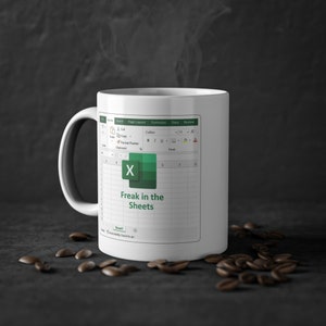 Può includere: Una tazza da caffè bianca con un design di foglio di calcolo Microsoft Excel verde e bianco. Il testo "Freak in the Sheets" è stampato sulla tazza.