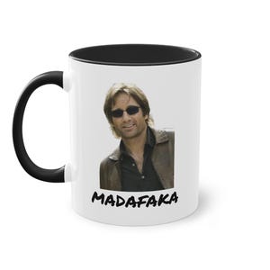 Könnte beinhalten: Weiße Keramik-Kaffeetasse mit schwarzem Rand und Henkel. Die Tasse zeigt ein Farbbild eines Mannes mit Sonnenbrille und Jacke. Der Text "MADAFAKA" ist in Schwarz am Boden der Tasse aufgedruckt.
