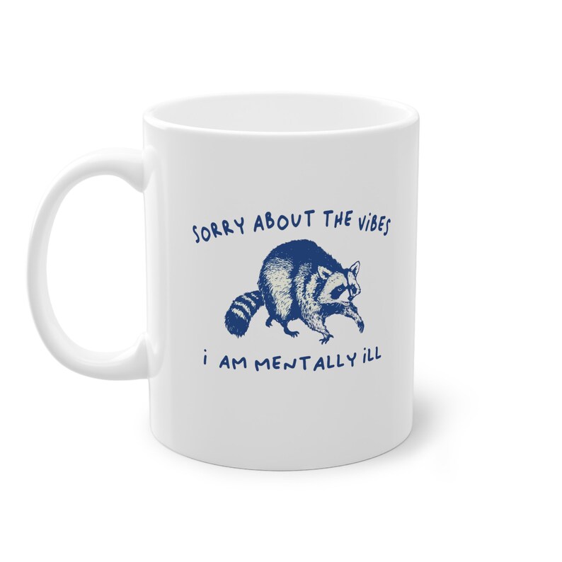 White ceramic mug with funny raccoon meme and caption Sorry About the Vibes, I Am Mentally Ill