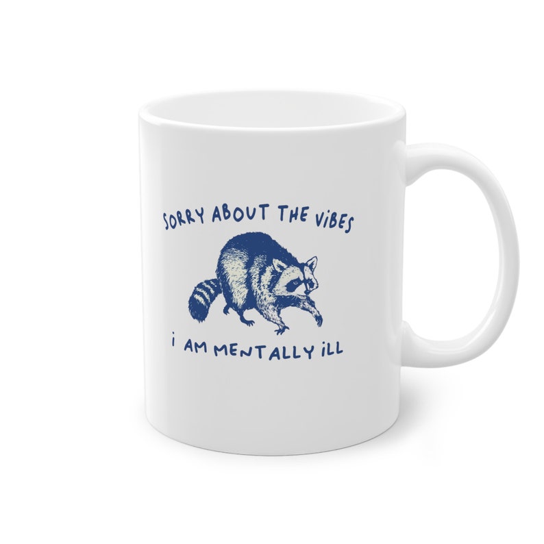 White ceramic mug with funny raccoon meme and caption Sorry About the Vibes, I Am Mentally Ill