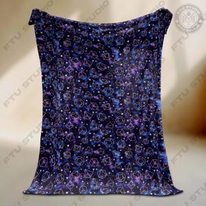 May include: A dark blue blanket with a repeating pattern of white geometric shapes, stars, and nebulas. The blanket has a soft, plush appearance and is likely made of a comfortable material. The design evokes a celestial theme, perfect for a bedroom or living room.