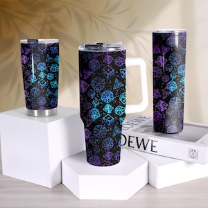 May include: Three insulated tumblers with a black background and a repeating pattern of dice in shades of blue and purple. The tumblers are displayed on white pedestals, with one tumbler featuring a white handle.