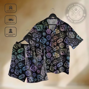 May include: Black button-down shirt and matching shorts set. The set features a repeating pattern of colorful dice on a black background. The dice are various shapes and sizes, with numbers visible on their faces. The shirt is short-sleeved, and the shorts have a drawstring.