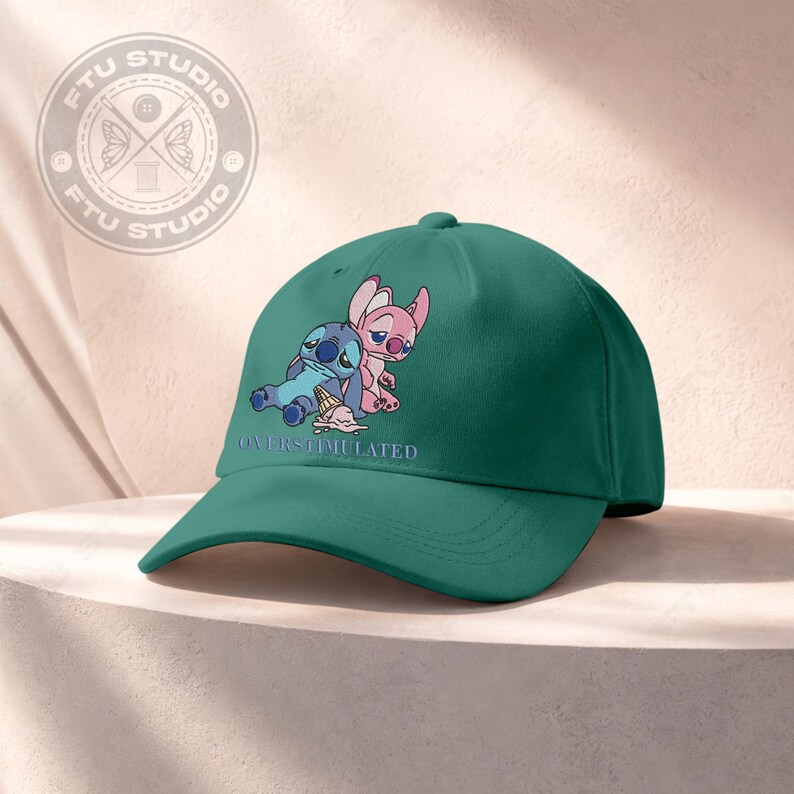 May include: A dark green baseball cap featuring a cartoon image of two characters, one blue and one pink, with the text "OVERSTIMULATED". The cap has a curved brim and a rounded crown, suitable for casual wear.