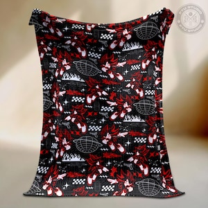Puede incluir: Manta negra con un patrón repetido de un personaje rojo, cuadrados blancos y negros a cuadros, estrellas blancas y un diseño de globo. La manta también presenta un diseño de llamas y pistolas.