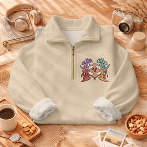 May include: Beige quarter-zip sweatshirt with a white fleece lining and a colorful embroidered design of four dragons playing a game at a table. The sweatshirt has a gold zipper and a relaxed fit.