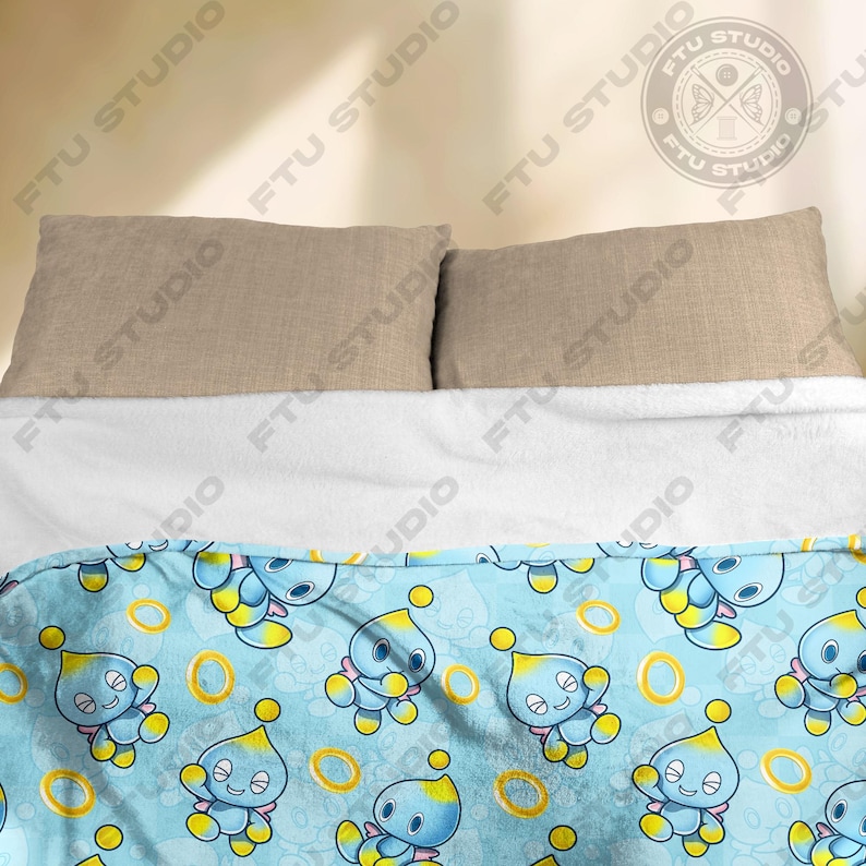 May include: A blue and yellow fleece blanket with a repeating pattern of a blue cartoon character with yellow eyes and a yellow ring. The character is on a light blue background with yellow rings.