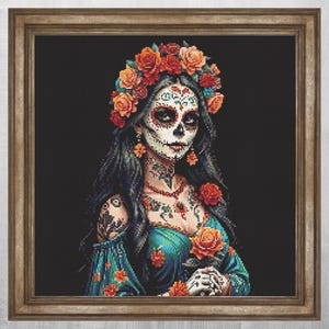Puede incluir: Retrato bordado enmarcado de una mujer al estilo de una calavera de azúcar del Día de Muertos. Lleva una corona floral, un vestido naranja y turquesa, y tiene intrincado arte facial y corporal. El fondo es negro.