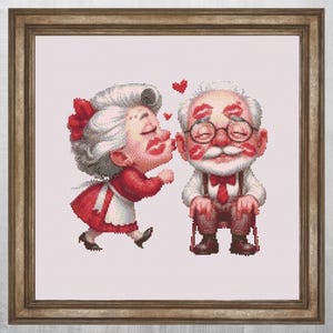 May include: A framed cross-stitch depicts an elderly couple in a loving embrace. The woman, in a red dress and apron, kisses the man, who is seated and covered in lipstick kisses. Red hearts float above them.