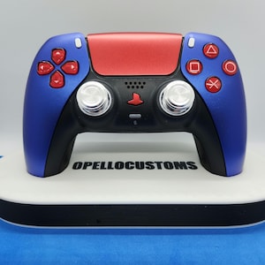 May include: A custom blue and red video game controller with red action buttons. The controller has a black center section with silver joysticks and the text "OPELLO CUSTOMS" on the base.