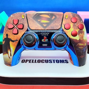 May include: A custom game controller featuring a Superman theme with a metallic blue finish, red buttons, and a central touchpad displaying the Superman logo. The controller includes graphics of Superman in flight and the text OPELLOCUSTOMS.