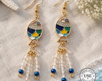 May include: Gold-tone fish earrings with blue, yellow, and green enamel details. The fish-shaped earrings have a crystal-studded top and dangle clear beads with blue accents. The earrings are designed with a hook closure.
