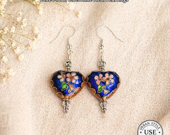 May include: Blue floral cloisonné heart earrings with silver-tone hooks and decorative accents. The earrings feature a dark blue enamel heart shape with floral designs in pink, green, and gold. The text "URBAN STYLE ESSENTIALS" is at the top.