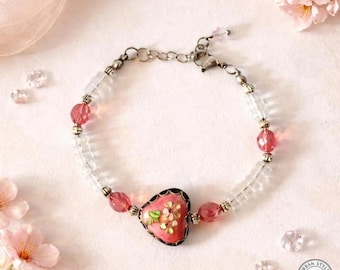 May include: A pink floral cloisonné heart bracelet. The bracelet features a heart-shaped pendant with a floral design, surrounded by pink beads and clear crystal beads. The text "URBAN STYLE ESSENTIALS" is at the top.
