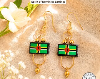 May include: Gold-toned earrings featuring the flag of Dominica. The rectangular pendants display the flag's green, yellow, black, and red design. The earrings have a hook closure and a small, round charm at the bottom. The text "Spirit of Dominica Earrings" is visible.