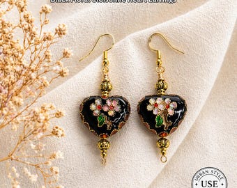 May include: Black floral cloisonné heart earrings with gold-colored hooks and accents. The earrings feature a black heart shape with a floral design in pink, white, and green. The text "URBAN STYLE ESSENTIALS" is at the top.