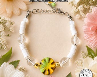 May include: A white and clear beaded bracelet with a central yellow and green circular charm. The bracelet has the text "Sundial Horizontal Bracelet" and "Urban Style Essentials". The bracelet is surrounded by flowers.