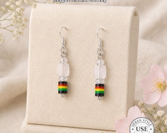 May include: A pair of earrings with a reggae theme. The earrings have a silver hook, clear beads, and a cylindrical bead with red, yellow, and green stripes. The text "Urban Style Essentials" and "Reggae Riddim Earring" are visible.