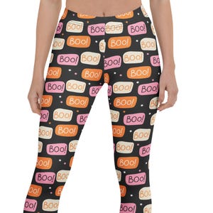 May include: Full-length leggings featuring a black background with a repeating pattern of rectangular speech bubbles in orange, pink, and cream. Each bubble contains the text "Boo!" in a dark font. Small white dots are scattered between the bubbles.