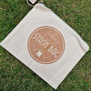 May include: A white canvas zippered pouch with a brown circle logo that says "Julie's Stash Bag" with a stylized image of a spool of thread and needles.