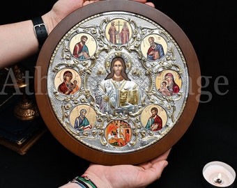 May include: A round wooden framed icon with a silver background and gold accents. The icon features a central image of Jesus Christ surrounded by eight smaller icons of saints. The icon is a traditional religious art piece.