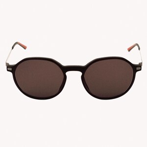 Könnte beinhalten: Runde, schwarze Sonnenbrille mit dunklen Gläsern. Die Fassung ist mattschwarz, mit silberfarbenen Bügeln und roten Akzenten an den Bügelenden. Klassisches, minimalistisches Design.