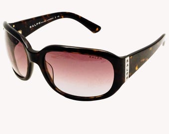 Peut inclure: Lunettes de soleil marron foncé à motif écaille de tortue avec verres roses dégradés. Les lunettes ont une monture arrondie et la marque "RALPH" est visible sur les branches et les verres.