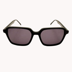 Op de afbeelding: Zwarte zonnebril met een vierkant montuur en donkere glazen. De zonnebril heeft een modern design met een strakke, minimalistische uitstraling. De monturen zijn dik en de glazen zijn donkergrijs.