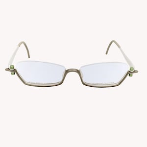 Op de afbeelding: Bril zonder montuur met een lichtbruin montuur en heldere glazen. De veren zijn wit met gebogen uiteinden. Het montuur heeft groene accenten bij de scharnieren. Tekst op de glazen luidt "2 lens shapes available" en "Prodesign Denmark".