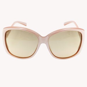 Puede incluir: Gafas de sol rosas pálido de gran tamaño con lentes doradas. Las monturas tienen forma de ojo de gato redondeado. Las patillas son de color rosa pálido a juego. Estas gafas ofrecen un look vintage elegante.