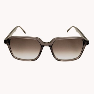 May include: Grey square-framed sunglasses with gradient brown lenses. The sunglasses have a modern, geometric design with a slightly oversized fit. The frames are a translucent grey colour, and the lenses transition from a dark brown at the top to a lighter shade at the bottom.