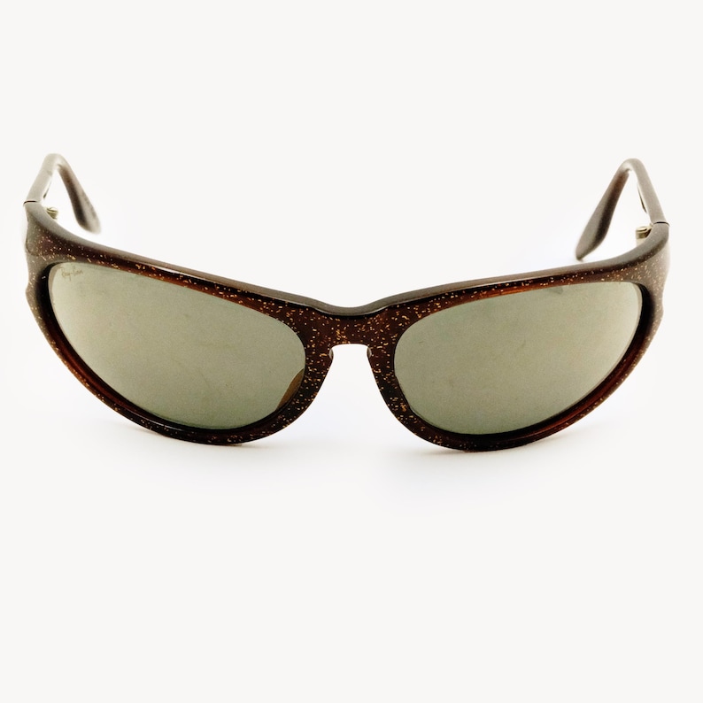 May include: Brown speckled sunglasses with gray lenses. The sunglasses have a curved frame and dark brown arms. The lenses are oval-shaped and the frame has a speckled pattern.