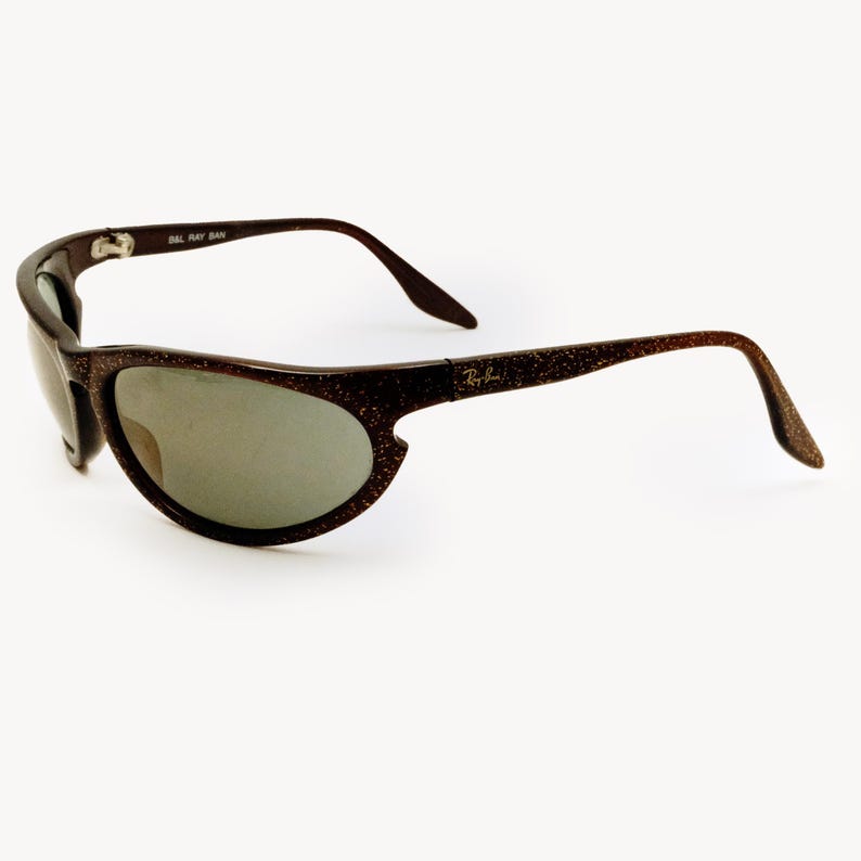 May include: Brown speckled sunglasses with a curved frame and gray lenses. The Ray-Ban logo is visible on the right arm. The sunglasses have a sporty, wraparound design.