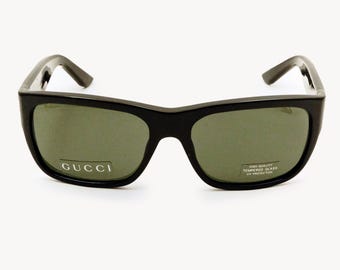 Może przedstawiać: Czarne okulary przeciwsłoneczne z zielonymi soczewkami. Okulary mają prostokątną oprawkę, a nazwa marki "GUCCI" jest widoczna na lewej soczewce. Naklejka na prawej soczewce głosi "HIGH QUALITY TEMPERED GLASS UV PROTECTION."
