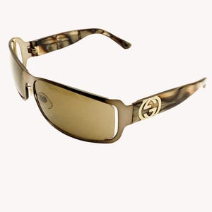 May include: Brown-tinted sunglasses with a rectangular frame. The temples feature a marbled pattern and a gold-colored logo. The sunglasses have a sleek, modern design.