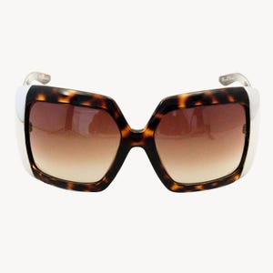 Può includere: Occhiali da sole oversize con montatura a fantasia tartarugata e lenti sfumate marroni. Le aste sono bianche con dettagli argentati. Questi occhiali offrono un look audace e alla moda.