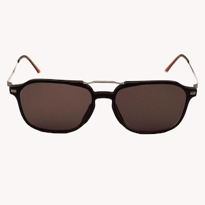 Puede incluir: Gafas de sol negras con lentes oscuras. Las monturas son de color negro mate con un puente plateado y detalles rojos en las patillas. Las lentes son de color oscuro y sólido, proporcionando un aspecto elegante y moderno.