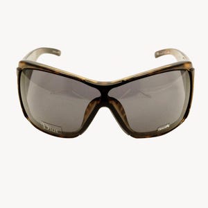 May include: Brown and black oversized sunglasses with gray lenses. The sunglasses have a thick frame with a tortoiseshell pattern. The Dior logo is visible on the left lens.