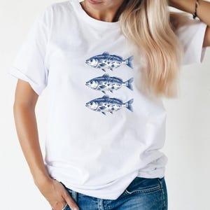 May include: White t-shirt with a blue and white design of three fish swimming in a row.