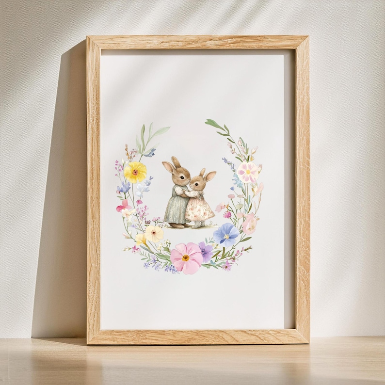 May include: A framed print of two brown rabbits hugging, surrounded by a wreath of colorful flowers. The rabbits are standing on a white background.