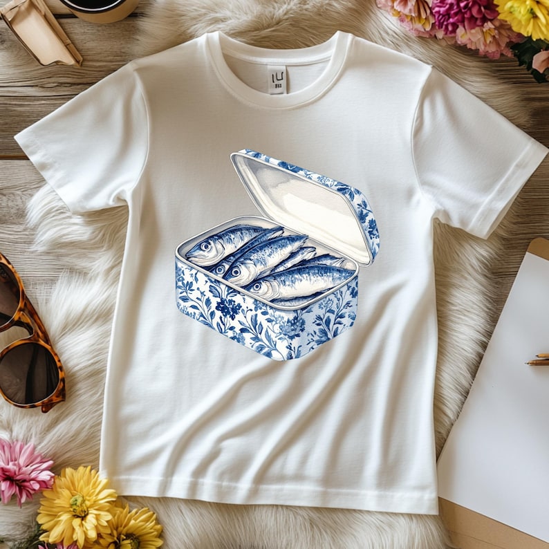 May include: White t-shirt with a blue and white illustration of a can of sardines. The can is open and the sardines are visible inside.