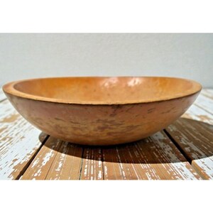May include: A handcrafted, oval-shaped bowl with a warm, earthy tone. The bowl has a smooth interior and a slightly textured exterior, showcasing natural variations in color. The bowl is likely made of wood or a similar material.