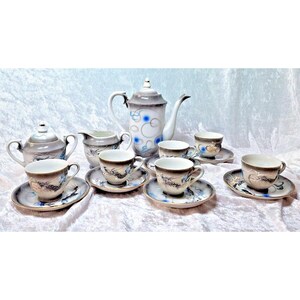 May include: A porcelain tea set featuring a teapot, a lidded sugar bowl, a creamer, and four teacups with matching saucers. Each piece displays a grey gradient finish with blue circular accents and detailed black dragon illustrations.