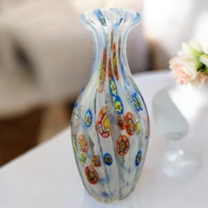 May include: A decorative glass vase with a flared top and a bulbous body. The vase is clear with a white, blue, yellow, and red floral pattern. The vase is approximately 8 inches tall.