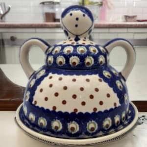 Op de afbeelding: Een keramische botervloot met een blauw en wit bloemmotief. De schaal heeft een ronde basis en een gewelfd deksel met een handvat. Het deksel is versierd met een patroon van pauwenveren en stippen. De schaal heeft een diameter van ongeveer 15 cm.