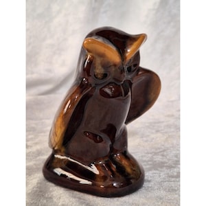 May include: A ceramic owl figurine in shades of brown and tan. The owl has a glossy finish and is perched on a small base. The figurine has detailed features, including large eyes and a curved beak. The owl is a decorative item.